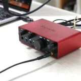 Scarlett Solo (gen. 4) がノートパソコンと接続され、マイクケーブルやヘッドホンが接続された状態。前面パネルのLEDが点灯している様子。