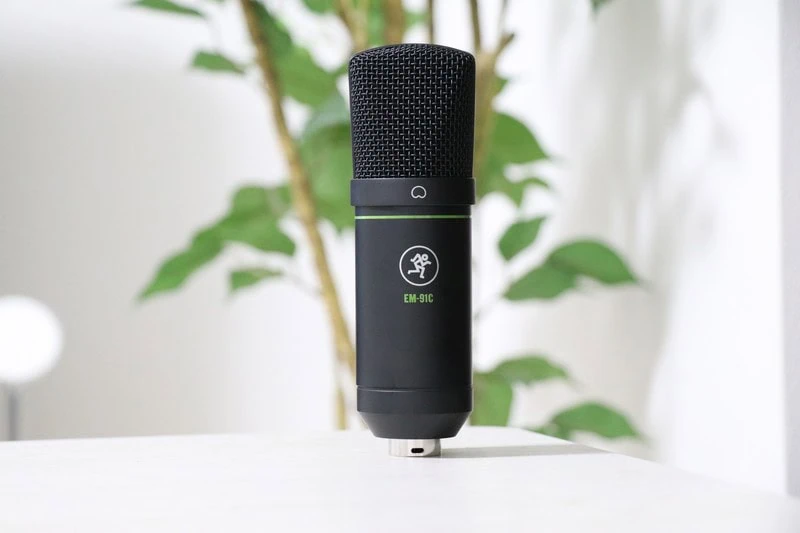 観葉植物を背景に、黒色のMackie EM-91Cコンデンサーマイクを正面から撮影した商品イメージ